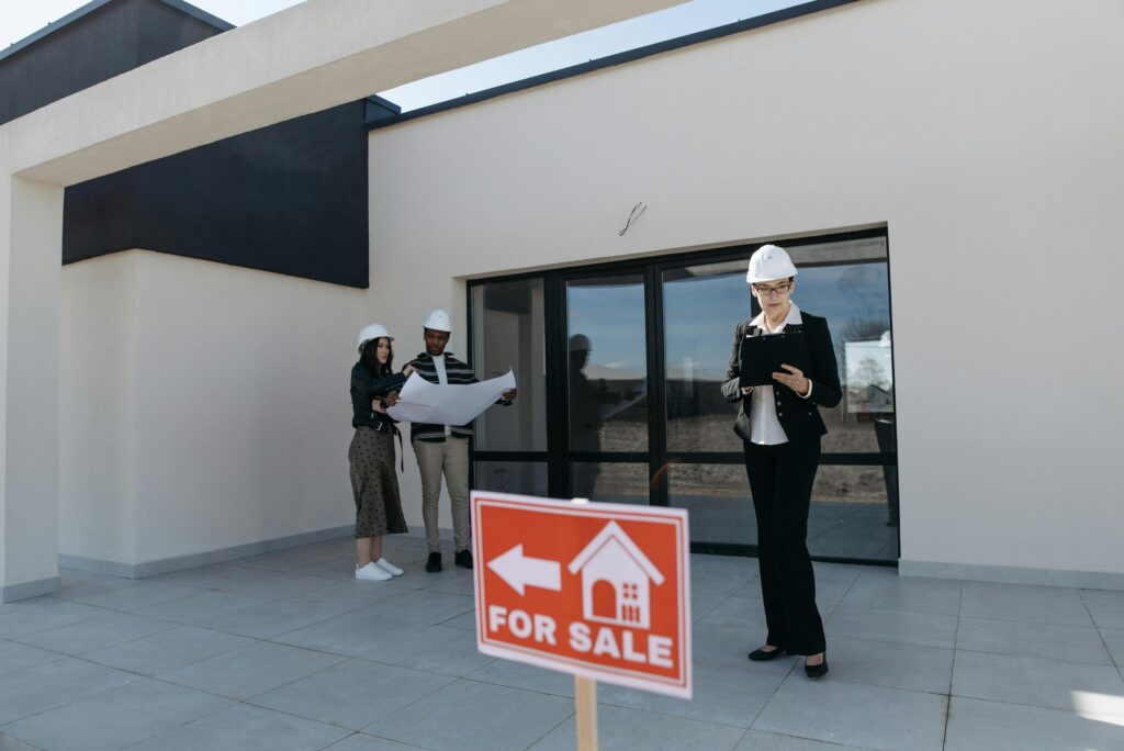 People with construction hats in front of a building with for sale sign