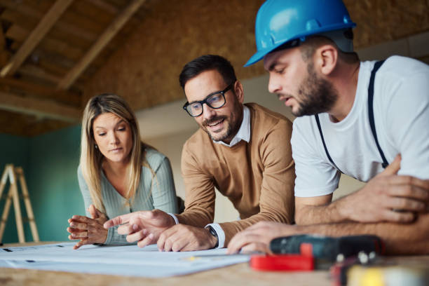 Young couple and their contractor cooperating while examining housing plan at construction site
